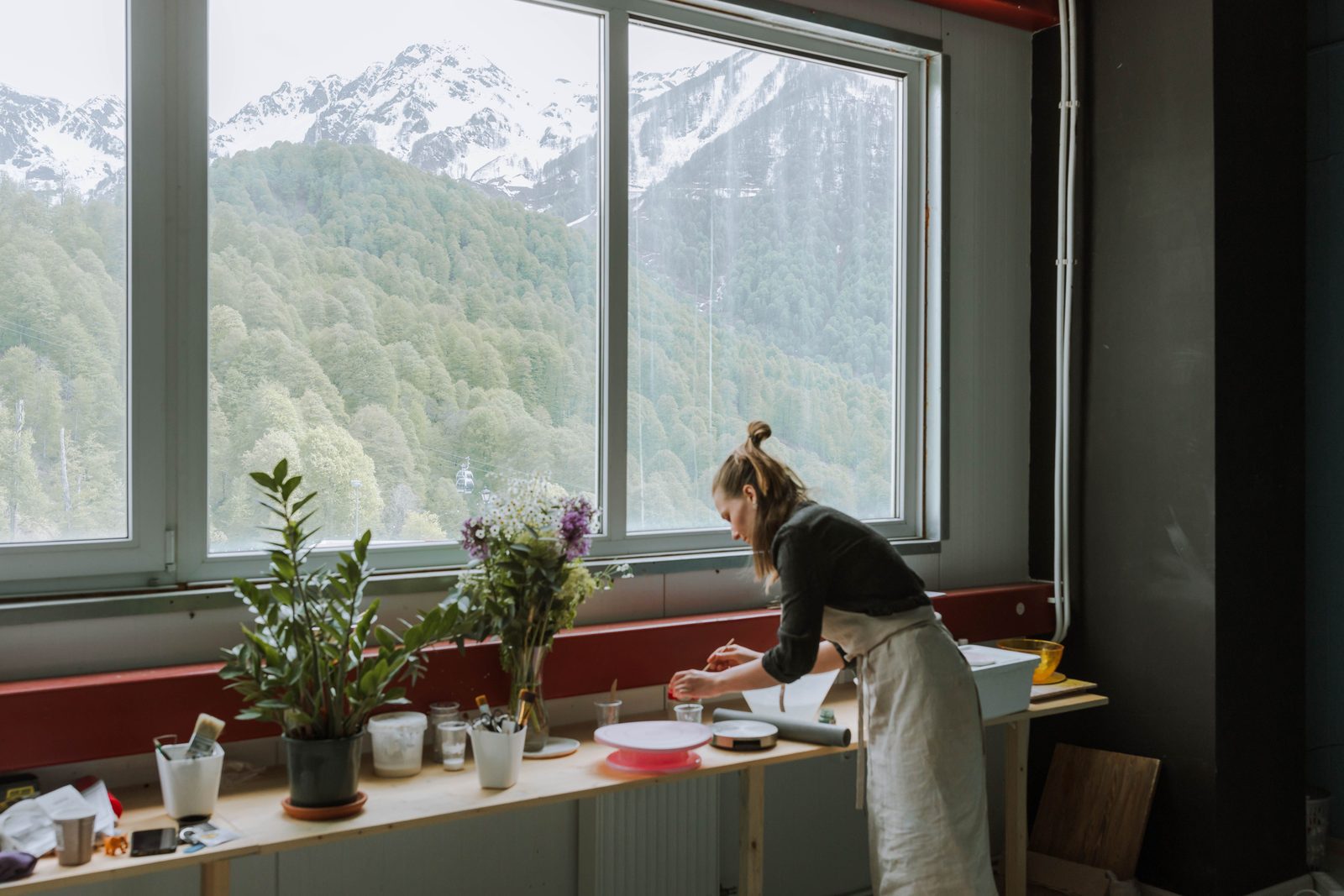 Floristin arbeitet in ihrem Atelier an einem langen Tisch vor einem Fenster mit Blick auf die Berge